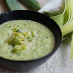 a black bowl filled with broccoli soup on top of a white table cloth