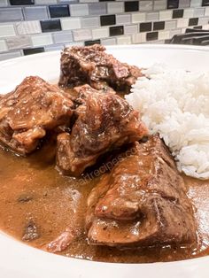 a white plate topped with meat and rice covered in gravy on top of a counter