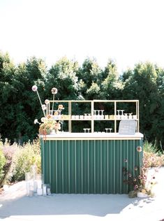 an outdoor bar made out of metal and green corrugated with flowers on the roof, surrounded by greenery