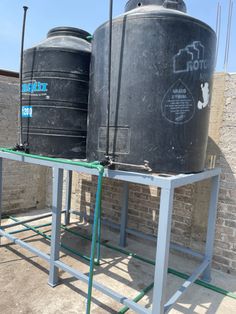 two large black tanks sitting next to each other on a metal stand in front of a brick wall