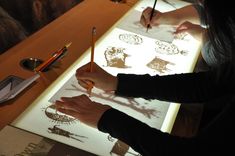 two people are drawing on paper with pencils at a table in front of them