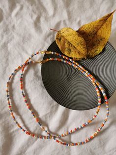 a yellow leaf sitting on top of a black plate next to a beaded necklace