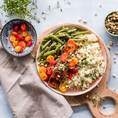 two bowls filled with vegetables and rice on top of a wooden cutting board next to a napkin