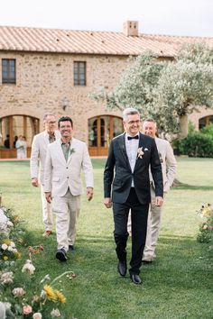 two men in tuxedos are walking down the aisle with other men behind them