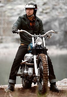 a man riding on the back of a motorcycle down a dirt road next to a river