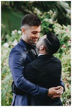 a man in a tuxedo hugs another man's face as they stand close to each other