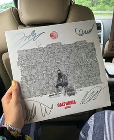 someone holding up a signed poster in the back seat of a car