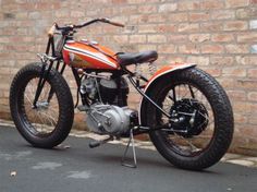 an orange and black motorcycle parked on the side of a road next to a brick wall