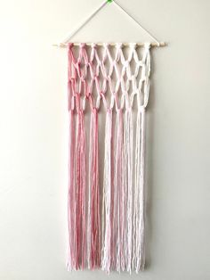 the wall hanging is decorated with pink and white yarn