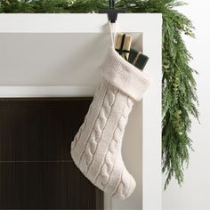 a christmas stocking hanging from the side of a fireplace with evergreen branches around it