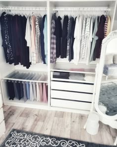 a white closet filled with lots of clothes and drawers next to a mirror on top of a wooden floor