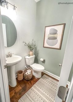 a white toilet sitting next to a sink in a bathroom under a framed art on the wall