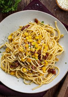 a white bowl filled with pasta and corn on top of a wooden table next to some parmesan cheese