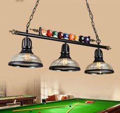 three lights hanging from the ceiling above a pool table with billiards on it