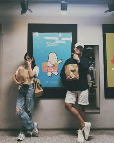 two people standing next to each other in front of a wall with posters on it