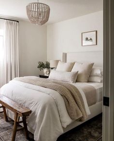 a bedroom with a white bed and wooden bench in front of the window, along with a chandelier