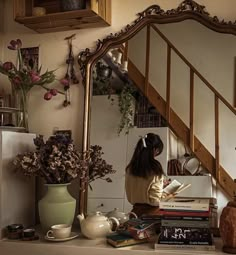 a woman sitting at a table with books and flowers in front of a large mirror