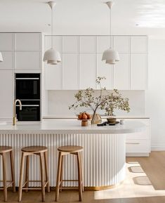 a white kitchen with three stools next to the counter and an island in front of it