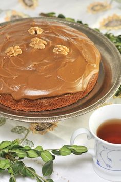 a cake on a plate next to a cup of tea and saucer with leaves