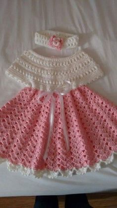 a crocheted baby dress and hat are on a bed with someone's feet