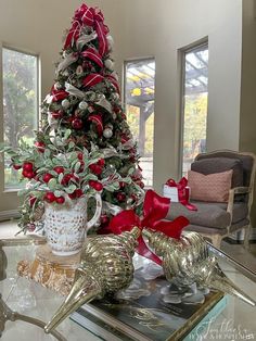 a decorated christmas tree in a living room with red and silver ornaments on the coffee table