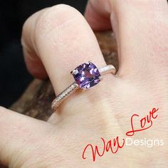 a woman's hand holding a ring with a purple stone and diamond on it