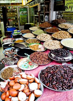 an outdoor market with lots of different types of food on display in bowls and pans