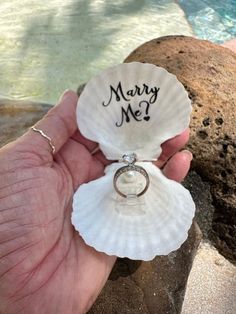 a person holding a shell with a wedding ring on it's finger next to a pool