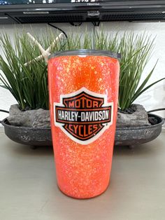 an orange glitter tumbler sitting on top of a table next to some plants and a television