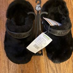 a pair of black furry slippers on top of a wooden floor next to scissors