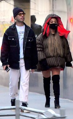 a man and woman walking down the street wearing masks