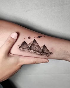 a woman's arm with tattoos on it and three pyramids in the background