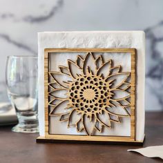 a wooden block with a laser cut sunflower on it sitting next to a glass of water