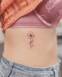 a woman's stomach with a small flower tattoo on her side ribcage