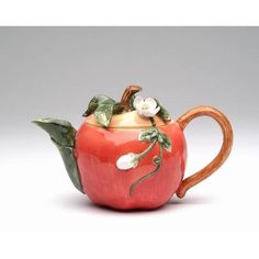 an apple shaped teapot with leaves and flowers on it