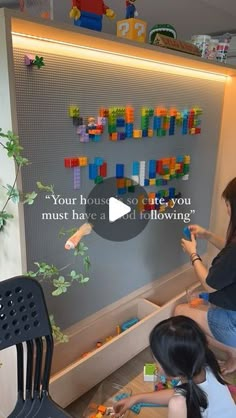 two girls are playing with legos in front of a wall mounted art piece that reads, your house must have a built - in following