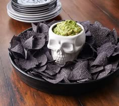 a plate with chips and guacamole in it on a wooden table next to stacks of plates