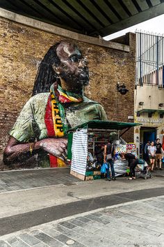 people are standing in front of a large mural on the side of a building that has a man's face painted on it