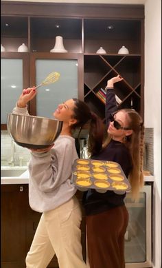 two women in the kitchen cooking cookies with a spatula on top of them and one holding a pan