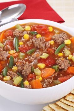 a white bowl filled with meat and vegetable soup next to crackers on a table