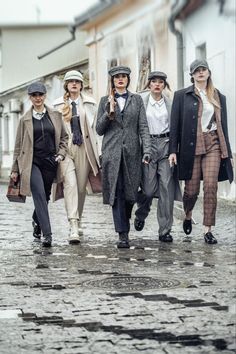 a group of people walking down a cobblestone street in hats and coats on