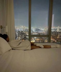 a woman laying in bed with her head on the pillow, looking out at city lights