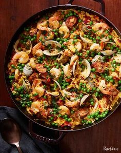 a skillet filled with shrimp, rice and peas on top of a wooden table