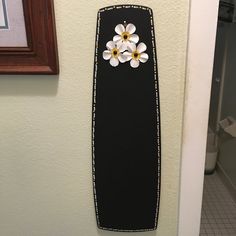 a black vase with white and yellow flowers on it next to a framed picture in a bathroom