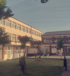 the building has many windows on it and is next to a sidewalk in front of some trees