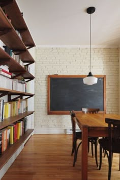 a wooden table with chairs in front of a chalkboard and bookshelves on the wall