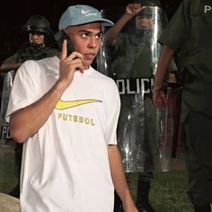 a young man talking on a cell phone while standing in front of police with his hand up to his ear