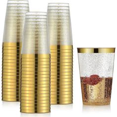 four gold colored cups and one glass with a strawberry on the bottom are next to each other