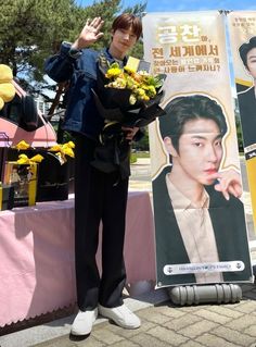 a man standing next to a poster holding flowers