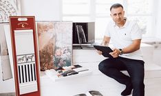 a man sitting on a window sill in front of a book shelf holding an ipad